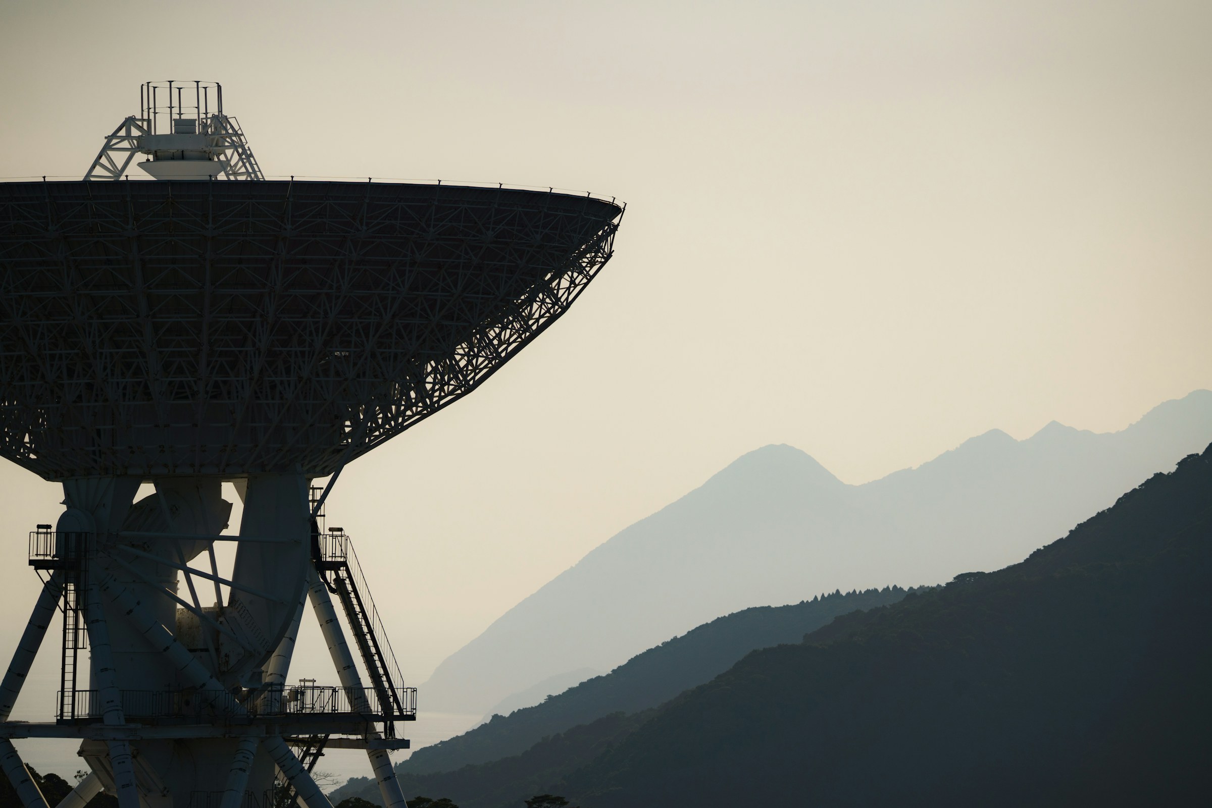 Large satellite ground station antenna in silhouette in front of misty mountains